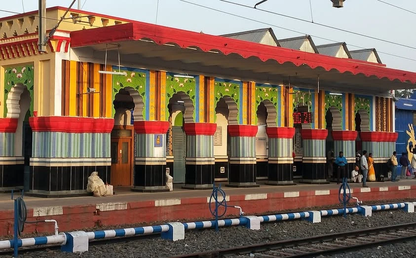 The vibrant platform of Bolpur Shantiniketan railway station, featuring arched pillars decorated with colorful stripes and traditional folk-art murals.
