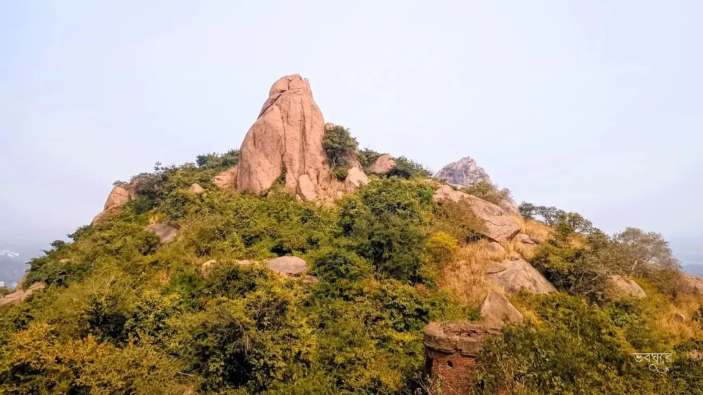 A majestic granite monolith of Joychandi Pahar in Purulia, West Bengal, featuring rugged rock formations, lush green vegetation, and a clear sky, famously known as a rock climbing destination and Satyajit Ray film location.