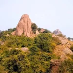 A majestic granite monolith of Joychandi Pahar in Purulia, West Bengal, featuring rugged rock formations, lush green vegetation, and a clear sky, famously known as a rock climbing destination and Satyajit Ray film location.