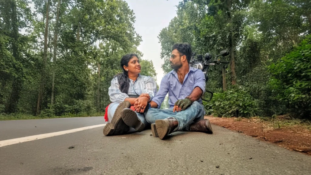 Shaown and Shilajeet, co-owners of Bhoboghure™, sitting on a forest road with a TVS Ronin motorcycle in the background during a road trip.