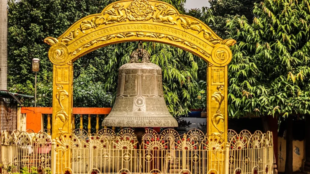 A large bronze ceremonial bell hanging under a golden ornamental arch with Buddhist symbols at Sarnath, near Varanasi.
