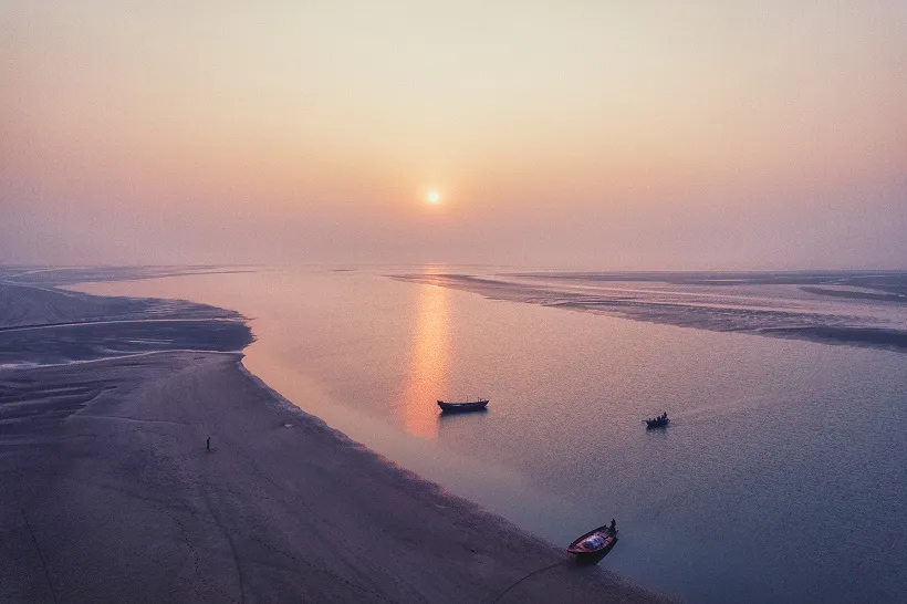 An aerial panoramic view of Talsari Beach in Odisha at sunrise, featuring traditional fishing boats on calm water with a golden sun reflection.